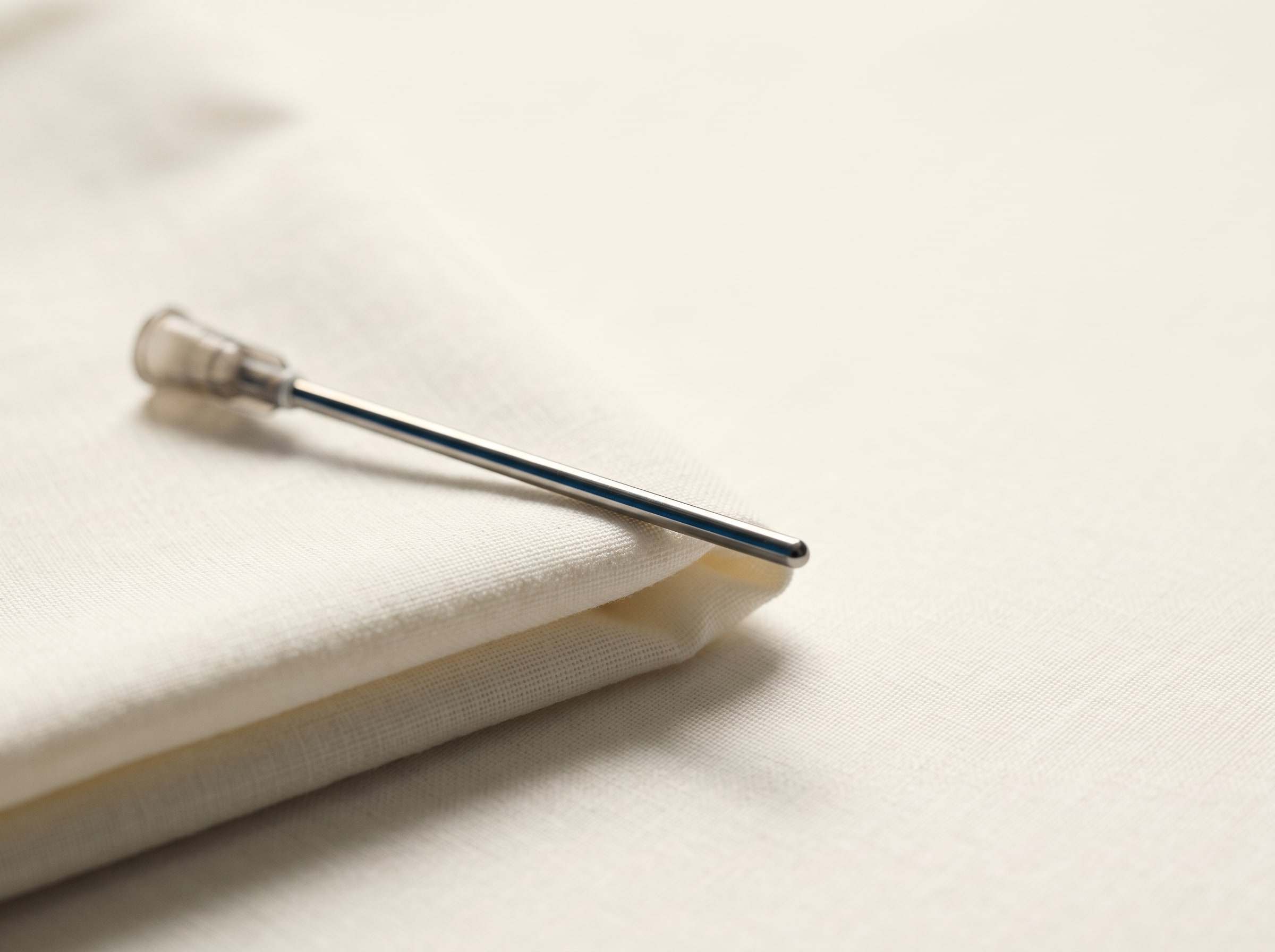A fine-gauge cannula resting on a folded ivory drape in soft daylight.